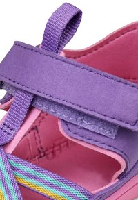 Scarpa in suede viola con interno rosa, caratterizzata da una fascia in Velcro e da accenti a righe multicolori sul lato. Design con punta aperta.