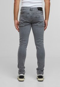 Vaqueros de mezclilla gris con corte slim, que presentan dos bolsillos traseros y un parche en la cintura, combinados con zapatillas negras y blancas.