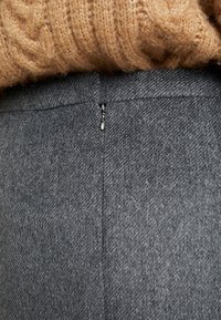 Lähikuva harmaasta villahameen vetoketjusta ja ruskean neulottu neulepaidon alareunasta.