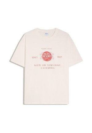 T-shirt écru à manches courtes avec texte et graphisme rouges indiquant « Pacific Resort Hotel West Coast, Since 1957, Where Time Slows Down California. »