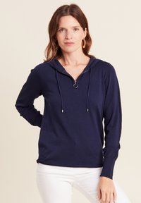 Marineblaue Kapuzenjacke mit einem Reißverschluss am Hals, Kordelzug und strukturierten seitlichen Einsätzen. Weicher Stoff mit langen Ärmeln, geradem Saum und silberner Hardware.