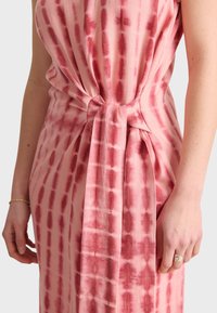 Vestido sin mangas en suave tejido rosa con un detalle de lazo en la cintura, que presenta un patrón de rayas rojizas y una textura lisa.