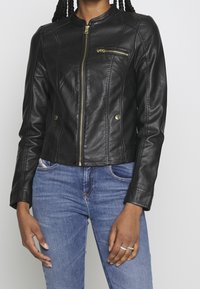 Czarna skórzana kurtka o dopasowanym kroju, z kieszenią na zamek na piersi, złotymi okuciami i teksturowanymi akcentami na ramionach.