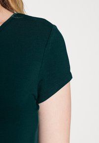 Ciemnozielona, krótko rękawowa koszulka z dekoltem w serek, wykonana z miękkiego materiału. Charakteryzuje się dopasowanym krojem z widocznymi detalami szwów.