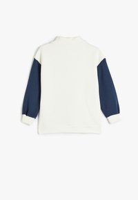 Suéter blanco con mangas azul marino, que presenta un cuello alto y puños acanalados. Textura suave, corte relajado y diseño minimalista.