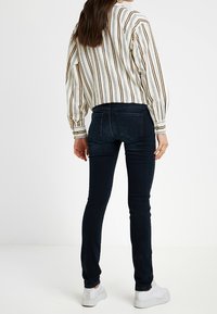 Mörkblå skinny jeans gjorda av denim, tillsammans med en vit randig blus. Har en figursydd design och subtila detaljer på bakfickorna.