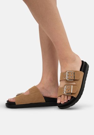 Brown suede sandals with dual silver buckles, open toe design, and a black rubber sole. Features a textured upper and flat base.