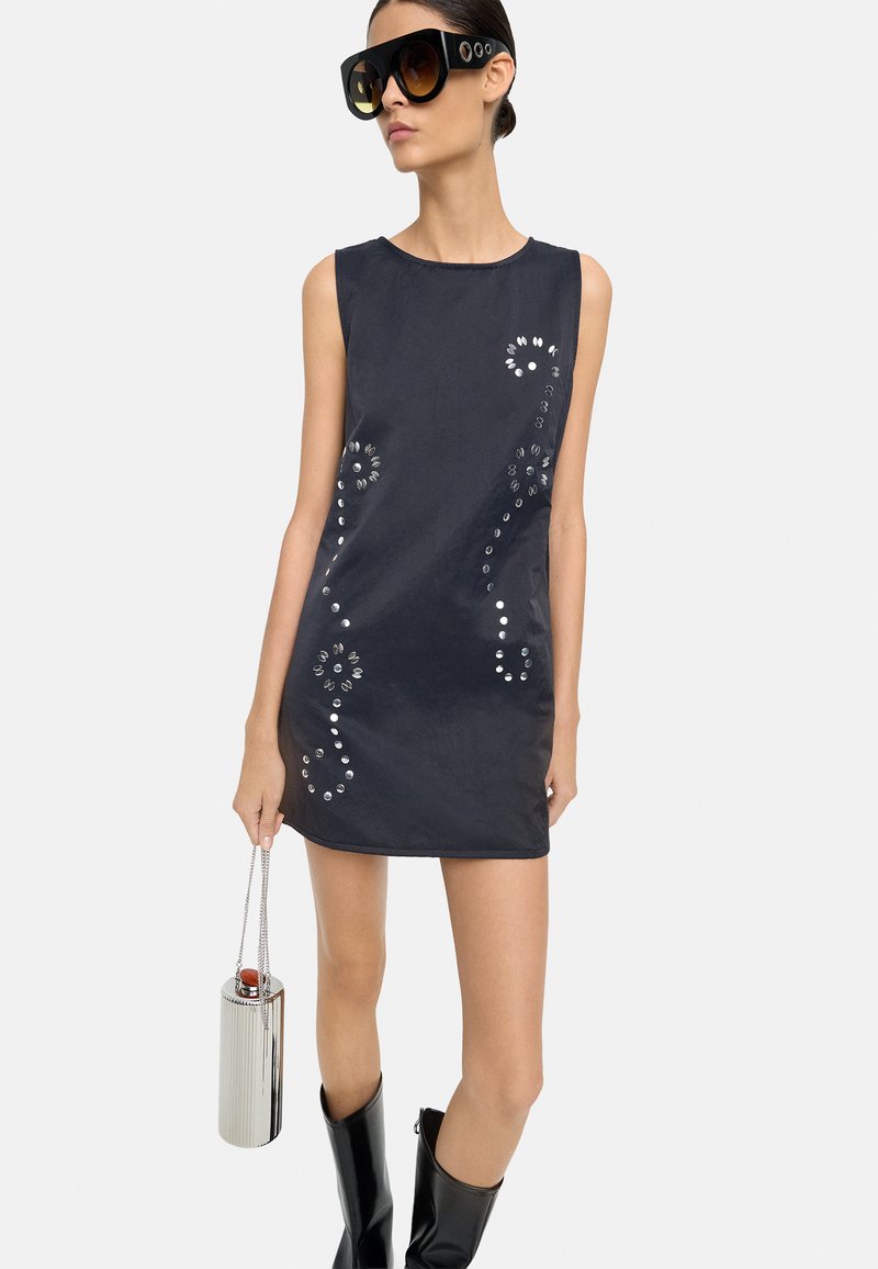 Bezramionna czarna mini sukienka z metalowymi ćwiekami w wirującym wzorze; zestawiona z błyszczącymi czarnymi kozaczkami do kolan i srebrną torebką.