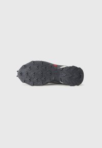 Talpa de pantof sport negru, robustă, cu modele de tracțiune proeminente, un accent roșu centrat și forme geometrice ridicate pentru aderență.
