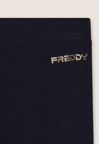 Leggings di un profondo blu navy realizzati in un tessuto morbido e elasticizzato, caratterizzati da un logo metallico oro "FREDDY" sull'anca e una cintura liscia.