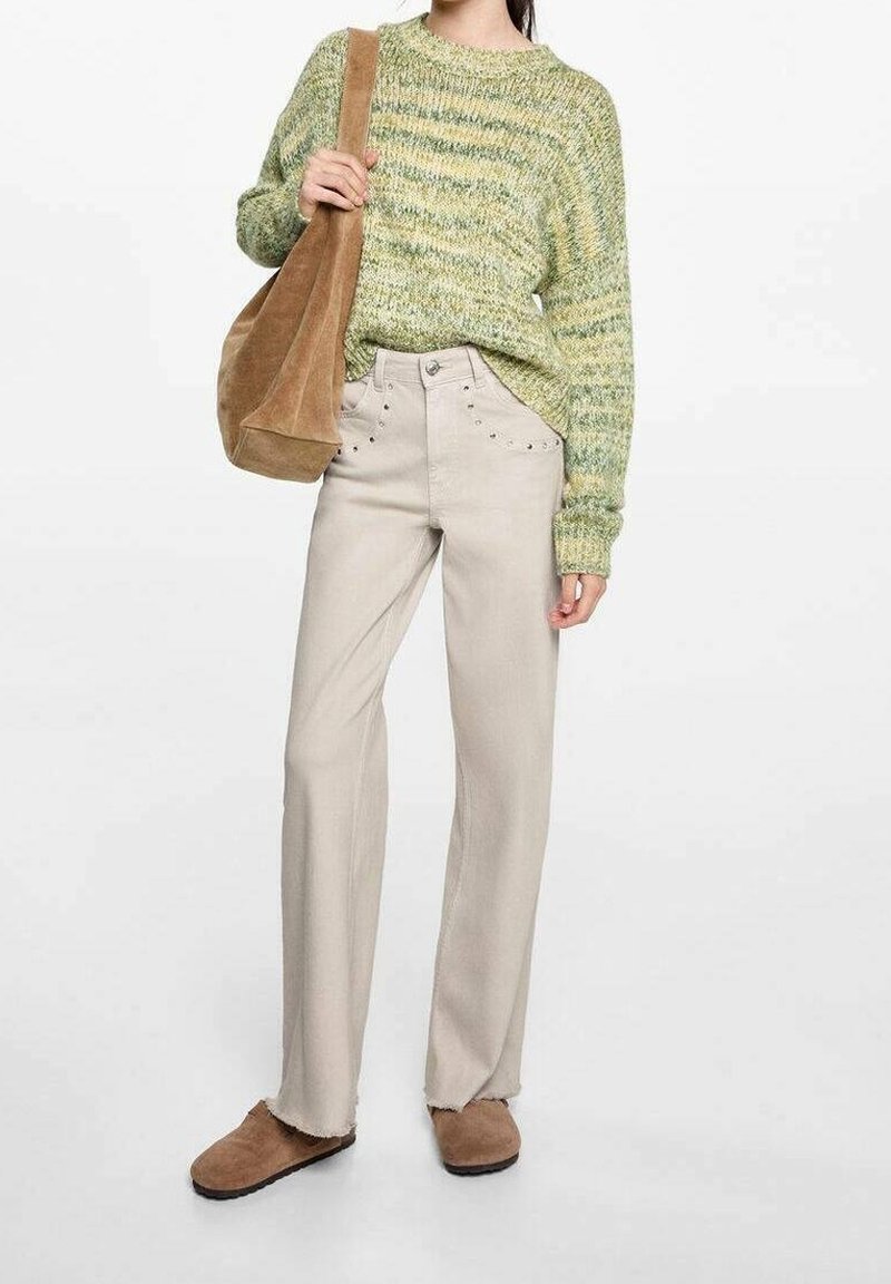 Femme portant un pull rayé vert, un pantalon beige à jambes larges avec des détails à clous, des chaussures en daim marron, et portant un sac à épaule en daim marron.