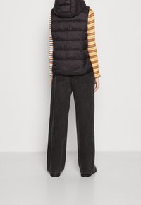 Zwarte puffer vest met capuchon, met een gestikt ontwerp, gedragen over een многekleurig gestreept T-shirt met lange mouwen en gecombineerd met een zwarte broek met brede pijpen.