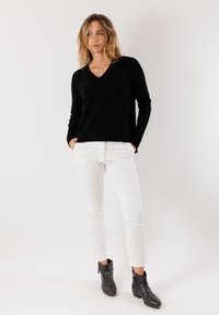 Maglione nero a V con maniche lunghe, abbinato a pantaloni bianchi attillati e stivali neri alla caviglia. Design semplice e texturizzato, senza motivi visibili.