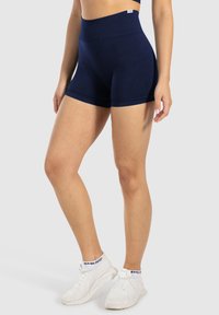 Marinblå hög midja atletiska shorts med en slät yta, som har ett brett midjeband och minimala sömmar, i kombination med vita träningsskor.
