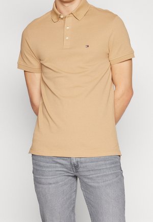 Polo beige en coton avec un col classique, une patte de boutonnage à trois boutons et un petit logo sur la poitrine. Manches courtes avec une finition soignée.