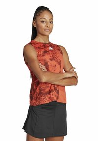 Top atlético sin mangas en un vibrante color rojo con un patrón texturizado, combinado con una falda negra. Tejido suave con un ajuste relajado.
