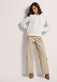 Lichte, crèmekleurige blouse met knopen bij de hals, gecombineerd met beige wijde broek met cargozakken en een enkellange zoom.