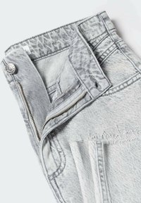 Jasnoszare szorty jeansowe z częściowo rozpiętym zamkiem błyskawicznym, zapinane na guzik, z postrzępionym wykończeniem, złożone na białym tle.