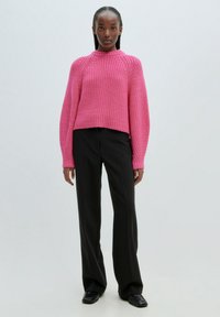 Pull en maille magenta avec un col montant, texture côtelée et épaules tombantes, associé à un pantalon noir taille haute et des chaussures noires.