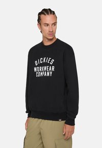 Black sweatshirt made of cotton, featuring white text that reads "DICKIES WORKWEAR COMPANY." Classic fit with ribbed cuffs and hem.
