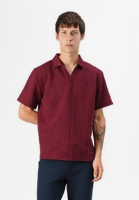 Polo shirt bordeaux à manches courtes avec un motif en losanges texturé, un col à trois boutons et une coupe décontractée. Tissu uni, mélange de coton.