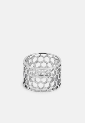 Bague en argent avec un motif en nid d'abeille composé de découpes hexagonales, présentée sur un fond clair uni.