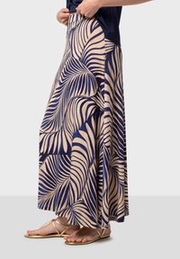 Maxikjol i krämfärg med marinblått palmbladsmönster, med flytande design och elastisk midjeresår, kombinerad med guldfärgade platta sandaler.