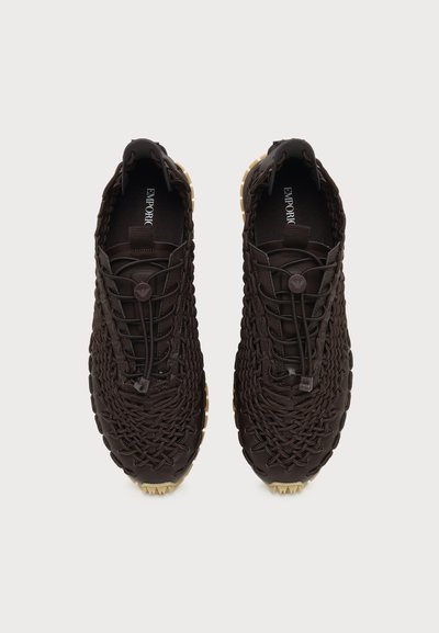 Paire de baskets tissées marron foncé avec des lacets élastiques et des semelles en caoutchouc beige, vues de dessus sur un fond clair uni.