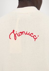 Kreminės spalvos mezgamos megztinis, išsiskiriantis minkšta tekstūra ir siuvinėtu raudonu logotipu ant nugaros. Laisvas kirpimas, lengva ir kvėpuojanti medžiaga.