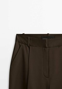 Pantalon habillé marron foncé avec passants de ceinture, poches latérales et ceinture plate devant.