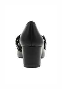 Chaussures à talons hauts noires avec un bout pointu, présentant une texture lisse, un talon empilé et une sangle décorative avec une boucle au niveau de la cheville.