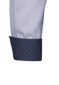 Mansica di camicia button-up in tessuto a quadretti azzurro chiaro con interno pattern blu scuro, caratterizzato da piccole croci blu e bianche.