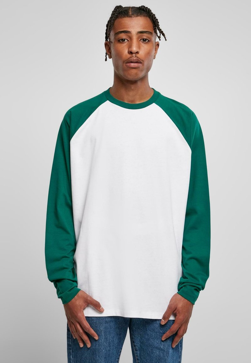 Langarm-Raglan-T-Shirt mit einem weißen Körper und grünen Ärmeln. Hergestellt aus Baumwolle, hat es einen Rundhalsausschnitt und eine lockere Passform. Auffällige Nahtdetails.