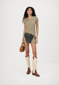 Beige, testre szabott póló, farmer foltvarrásos mini szoknya, barna kézitáska, fehér cowboy csizmák bonyolult mintázattal és téglalap alakú sarkakkal.