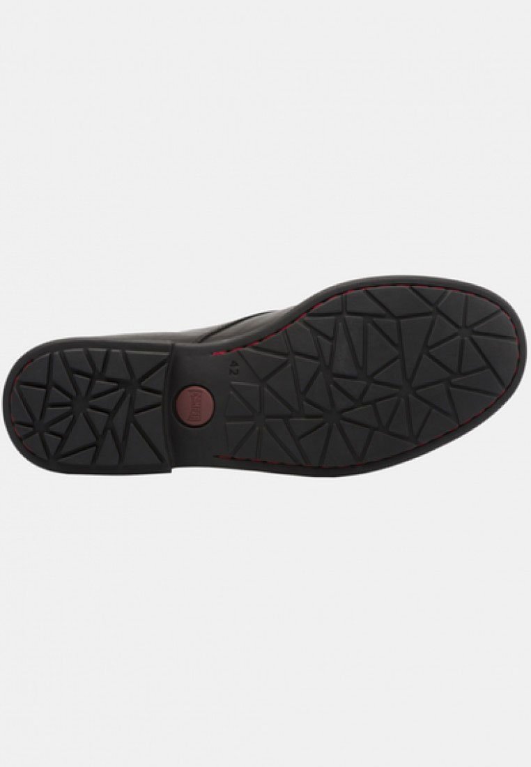 Schwarze Gummisohle mit strukturiertem Muster, das dreieckige Formen zeigt und einen roten Akzent am Rand besitzt. Zentrale Markeninschrift.