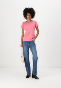 Pink short-sleeve t-shirt with rhinestone detail around the neckline, paired with light blue wide-leg jeans and black heeled boots.