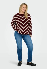 Maglione a righe bordeaux e crema con vestibilità ampia, scollatura rotonda e lavorazione a maglia testurizzata. Abbinato a jeans a gamba dritta blu chiaro e scarpe nere.