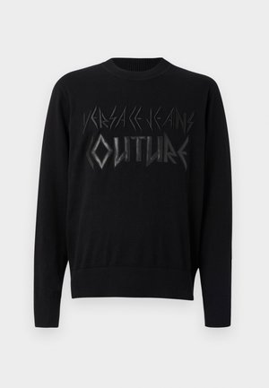 Musta neulepusero, jossa on voimakkaasti kohokuvioitu teksti kiiltävässä viimeistelyssä, pyöreä pääntie sekä ribbikuvioidut hihansuut ja helma.