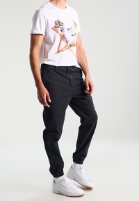 White t-shirt with a colorful koala graphic, paired with black tapered pants and white sneakers with tan accents.