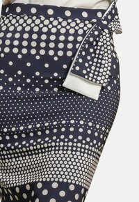 Falda lápiz azul marino con un patrón de puntos en crema, con un lazo lateral y una tela suave y texturizada.