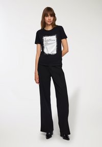 T-shirt in cotone nero con maniche corte, caratterizzato da una stampa grafica rettangolare bianca con testo. Abbinato a pantaloni ampi neri.