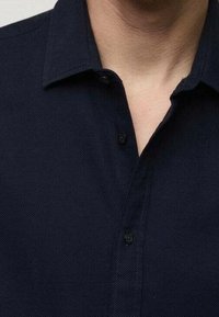 Camicia button-up di un blu scuro in tessuto texturizzato, con colletto a punta e una patta con bottoni neri.
