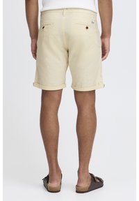 Beige katoenen shorts met omgeslagen boorden, twee achterzakken en een merklabel. Draagt met bruine slide-sandalen en heeft een eenvoudig ontwerp.
