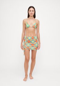 Set bikini con top a triangolo con motivo a scacchi arancione e turchese, abbinato a una gonna avvolgente coordinata con lacci laterali regolabili.