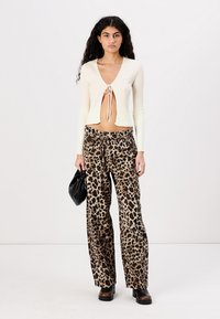White ribbed crop top with tie detail at the front, paired with loose leopard-print pants and dark heeled boots, holding a black bag.