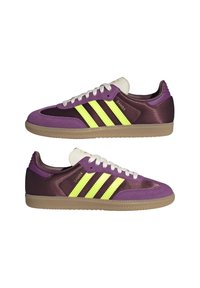 Sneaker viola e bordeaux scuro con tre strisce gialle vivaci, lacci bianchi, tomaia testurizzata e suola in gomma; design retro classico.