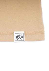 Beige bomuldsstof med en glat tekstur, der har et lille hvidt mærke med sort skrift og krydsede økser nær kanten.