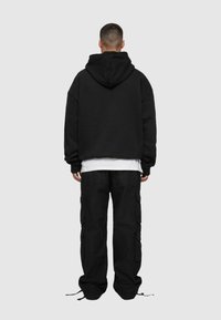Sort oversized hoodie med snor i hætten, kombineret med løse sorte cargo-bukser med flere lommer og elastiske manchetter.