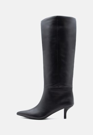 Botte haute pour femme en cuir noir, avec un bout pointu et un talon fin de hauteur moyenne, vue de profil sur un fond uni.