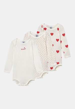 Trois bodies à manches longues pour bébé en coton blanc, avec des imprimés de cœurs rouges, des petits pois rouges et le texte "Petit Bateau" sur un des bodys.